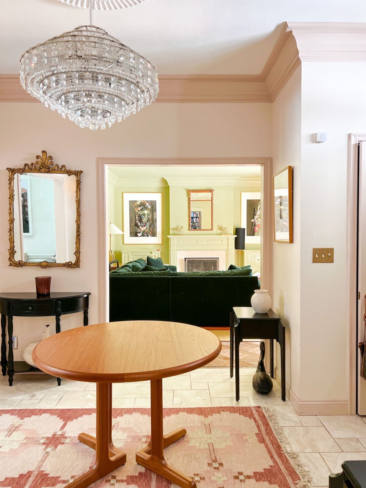 An entryway has cream walls and trim painted in Setting Plaster by Farrow & Ball. The room opens to a family room painted in a serene green color.