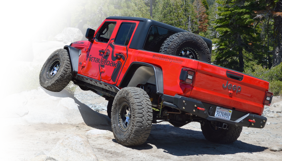 red jeep JT Gladiator with black MetalCloak decal on its side and black rocker rails driving over granite rocks on Rubicon Trail next to pine trees
