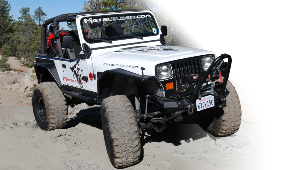 white Jeep YJ Wrangler with black and red MetalCloak wolf decal on the side and hood and black tow winch, driving on dusty path in the mountains near pine trees